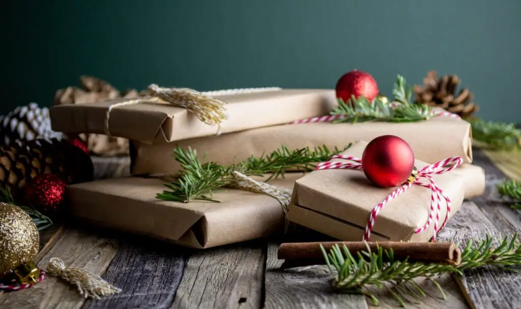 Arty photograph of 4 book-shaped christmas presents in brown paper, with a scattering of baubles and christmas tree branches
