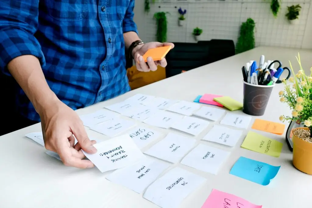 Close up of a person's hand sorting post-it notes on a white desk.