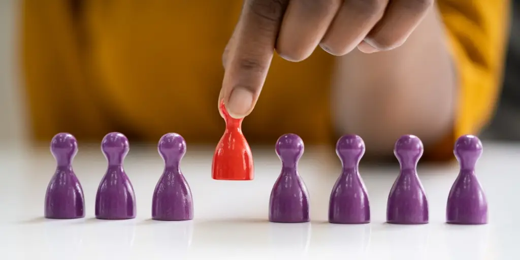 close up of 8 peg dolls, 7 in purple, one in red being picked up.