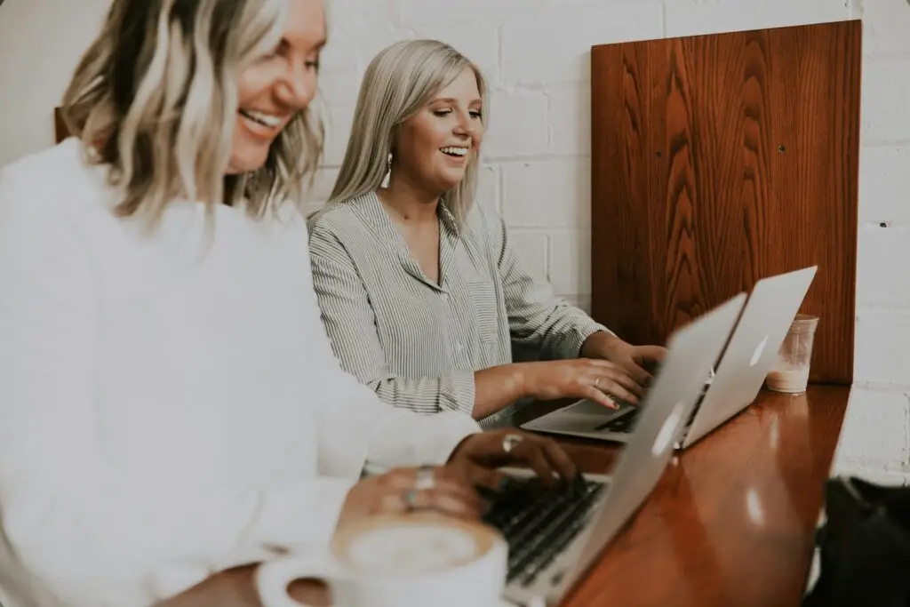 Close up of two smiling women working on laptops on a wooden desk