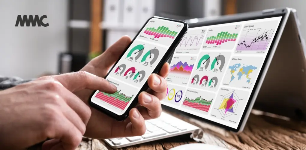 Close up of a laptop screen and smartphone screen with similar colourful metrics in graph form.