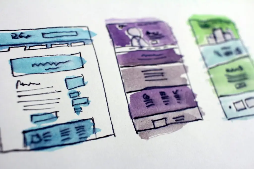 Close up photo of three sketches on paper in blue, purple and green, on white paper.