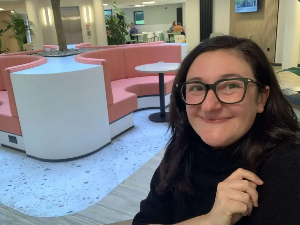 Selfie photo of employee, Sophie, who is smiling at the camera whilst in a shared office space environment.
