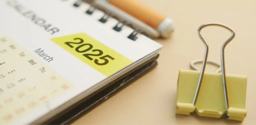 Close up photo of a pale yellow paper clasp next to the corner of a paper calendar showing March 2025