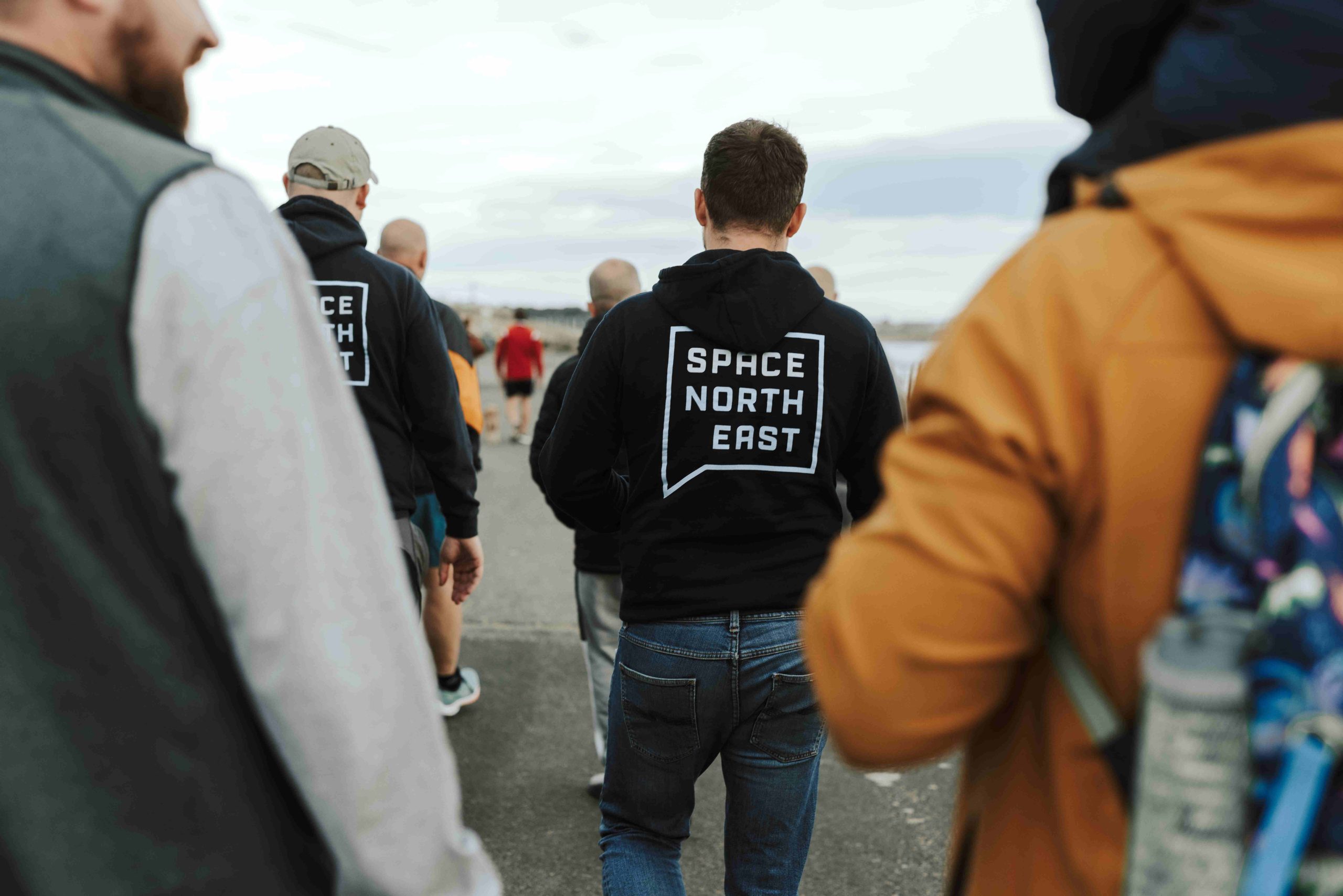 Photo of multiple men wearing coats, walking outside. The shot is from behind, and a close crop of the closest men.