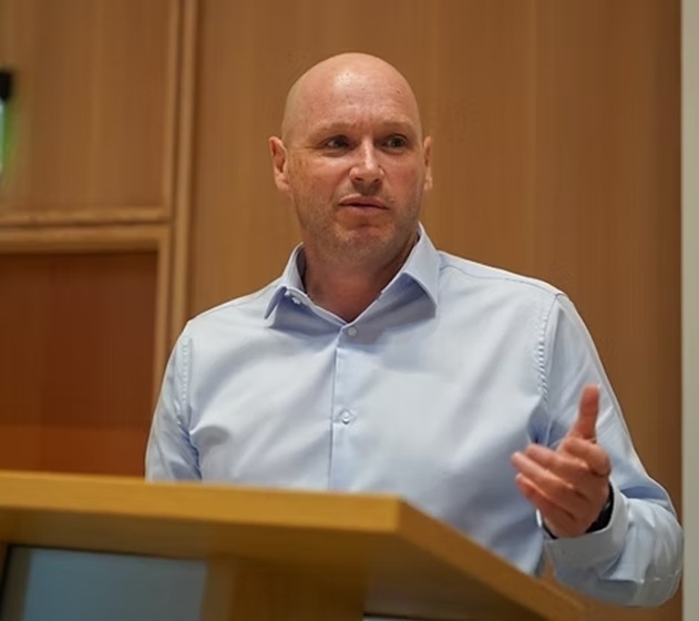 Photo of the owner of Is This You? from the waist up, standing at a pedestal, speaking at an event.