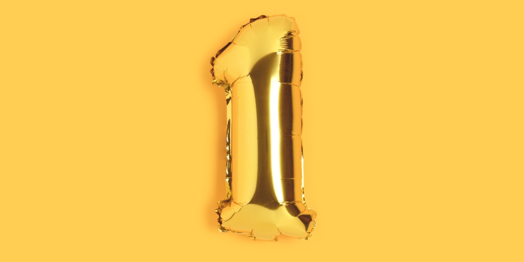 Bright gold number 1 foil balloon in the centre of a solid bright yellow background